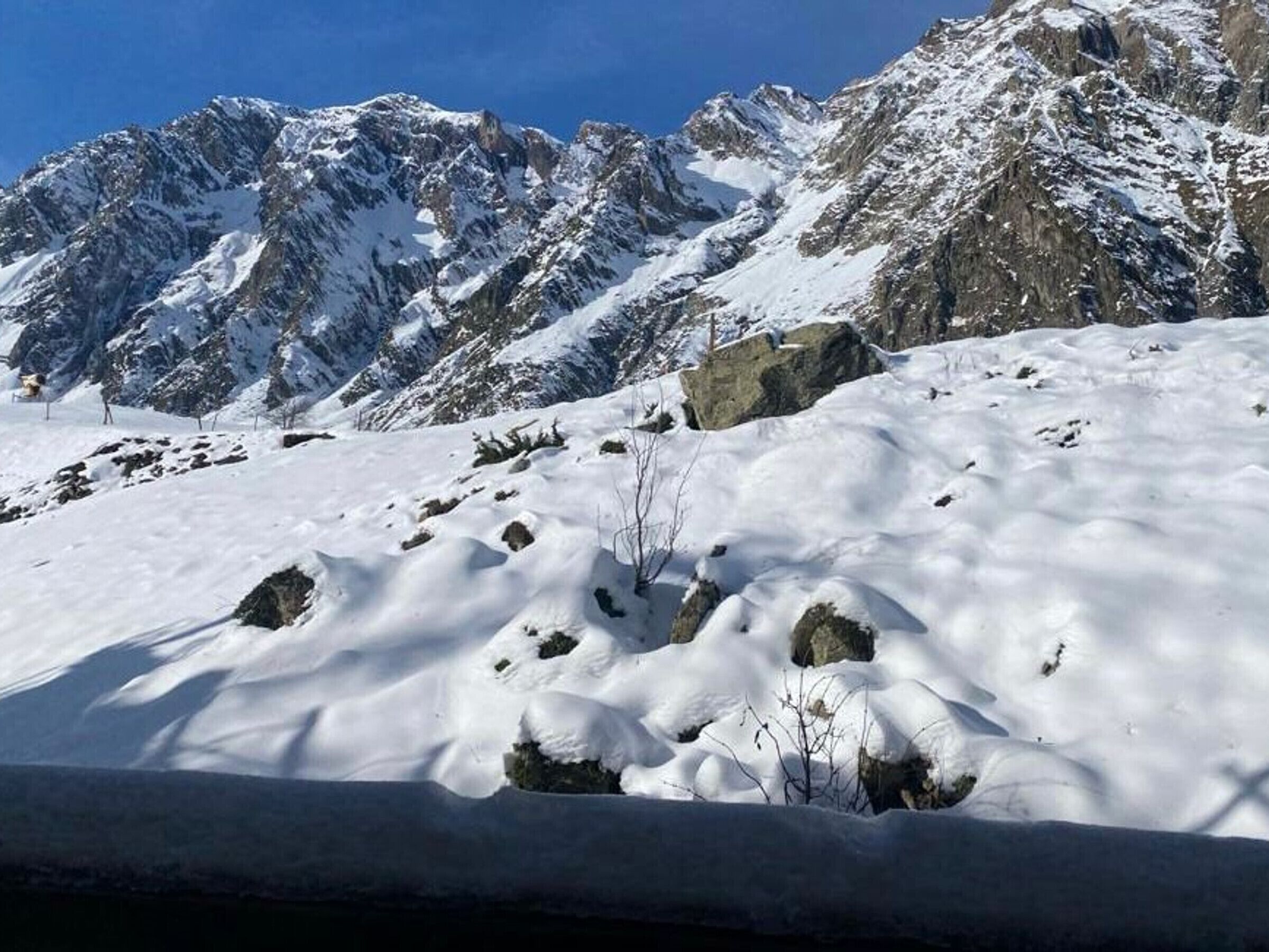 Un paysage montagneux enneigé, avec des affleurements rocheux et un ciel bleu dégagé.