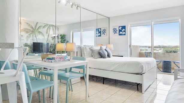 Une chambre d’hôtel avec un lit, un bureau et des chaises, une télévision et un balcon avec vue.