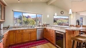 A modern kitchen with wooden cabinets, a stainless steel dishwasher, and a large window offering a view of a mountainous landscape. - Cathedral Views | Large home with two living spaces and kitchens (Sedona)