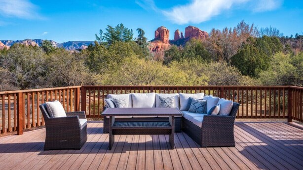 A deck with outdoor furniture, including a sofa and chairs, overlooking a scenic landscape with red rock formations and trees. - Cathedral Views | Large home with two living spaces and kitchens (Sedona)
