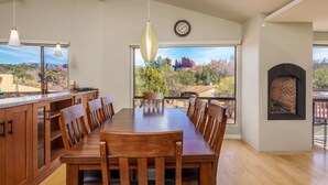 A spacious dining area with a long wooden table and chairs, a kitchen with wooden cabinets, and a fireplace. - Cathedral Views | Large home with two living spaces and kitchens (Sedona)