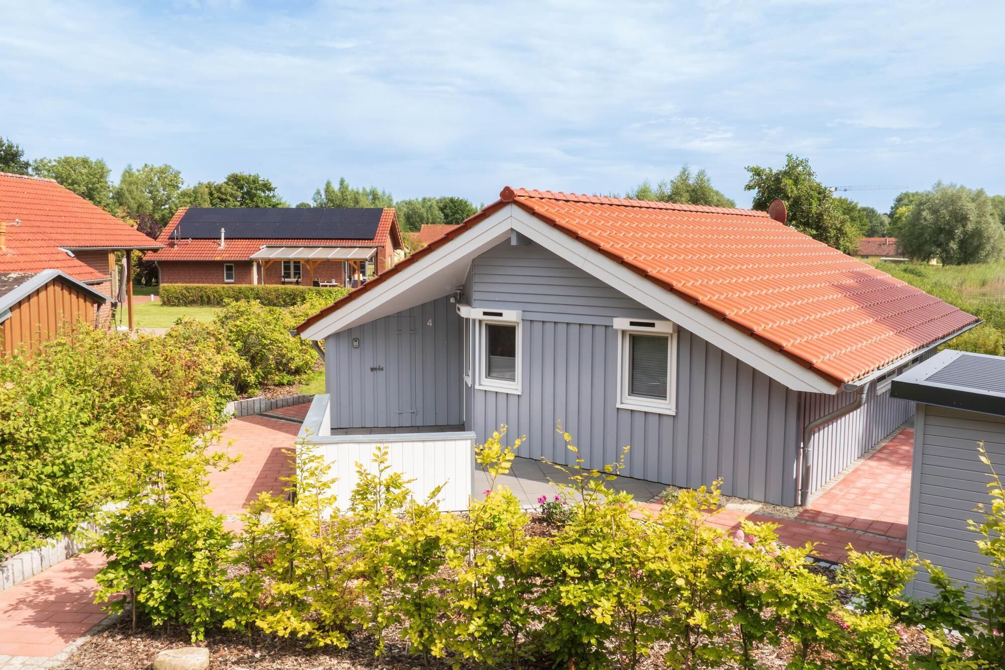 A small, single-story house with a red-tiled roof, a front porch, and a garden in front.