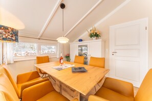 Uma sala de jantar com uma mesa de madeira, cadeiras laranjas, um lustre e um armário com portas de vidro.