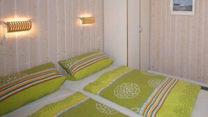 A room with wooden panel walls, a wardrobe, two beds with colorful bedding, and wall-mounted lighting.