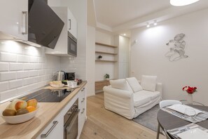 A modern kitchen with white cabinetry, a black range hood, and a dining area with a white sofa and a table set for two. - BnButler - Longhena, 7 (Milano)