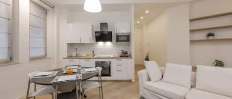 A modern kitchen with white cabinets, a dining table with chairs, and a white sofa.