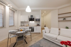 A modern kitchen with white cabinets, a dining table with chairs, and a white sofa. - BnButler - Longhena, 7 (Milano)