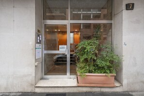 A building entrance with a glass door, a potted plant, and a number sign. - BnButler - Longhena, 7 (Milano)