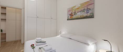 A bedroom with a bed, a bedside table, a lamp, a painting, and a wardrobe.