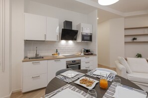 A modern kitchen with white cabinets, a built-in oven, and a dining area with a table set for two. - BnButler - Longhena, 7 (Milano)
