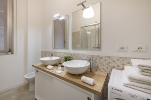 Une salle de bain avec deux lavabos, un miroir, un porte-serviettes et un lave-linge.