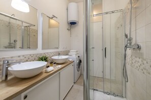 A modern bathroom with a large sink, a mirror, a washing machine, and a glass-enclosed shower. - BnButler - Longhena, 7 (Milano)