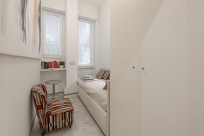 A small, well-lit room with a bed, a chair, a small table, and a bookshelf. - BnButler - Falcone, 5 - App. 2 (Milano)