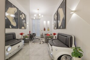 A modern living room with two vintage car sofas, a chandelier, and artwork on the walls.