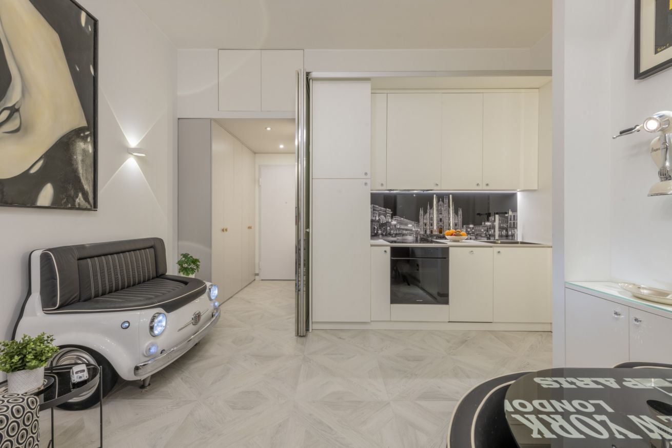 Une cuisine moderne avec des meubles blancs, un réfrigérateur et un coin repas doté d’une table au thème rétro automobile.