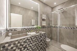 Een moderne badkamer met een douchecabine van glas, een grote spiegel en een betegelde spatwand met een patroon.