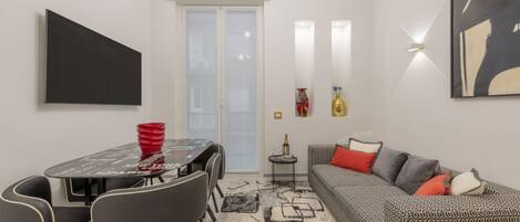 A modern living room with a dining table, chairs, a sofa, and a patterned rug.