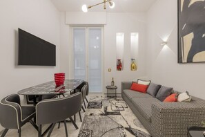 A modern living room with a dining table, chairs, a sofa, and a patterned rug.