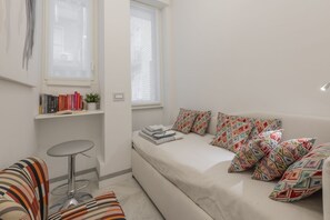 A small, modern room with a bed, a sofa, a small table, and a window.