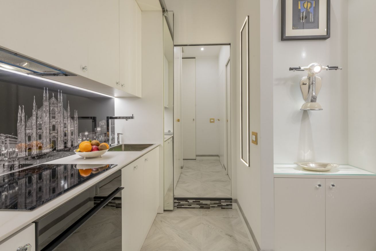 Una cocina moderna con una isla grande, un comedor con candelabro, y un pasillo que lleva a un baño.
