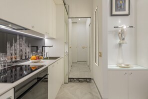 A modern kitchen with a large island, a dining area with a chandelier, and a hallway leading to a bathroom. - BnButler - Falcone, 5 - App. 2 (Milano)