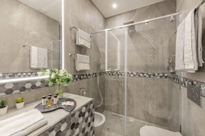 A modern bathroom with a glass-enclosed shower, a marble-tiled shower area, a glass shower door, a toilet, and a vanity with a mirror and a decorative tile backsplash.