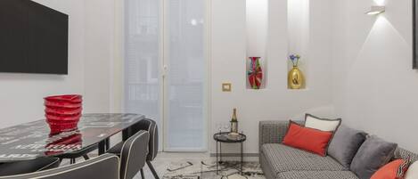 A modern living room with a sofa, a dining table with chairs, a TV, and a small side table with a vase.