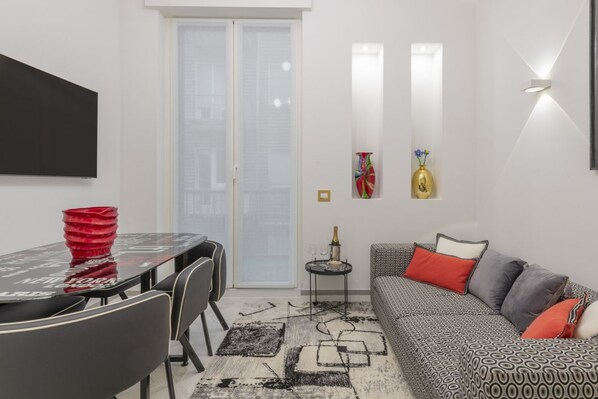 A modern living room with a sofa, a dining table with chairs, a TV, and a small side table with a vase. - BnButler - Falcone, 5 - App. 2 (Milano)