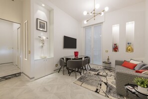 A modern living room with a dining area, a sofa, a TV, and a chandelier.