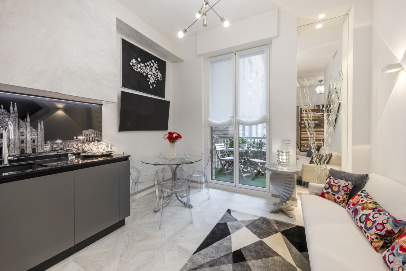 A modern kitchen with a dining area, a sofa, and a large window.