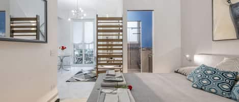 Un dormitorio moderno con cama, mesita de noche, espejo y vistas al exterior.