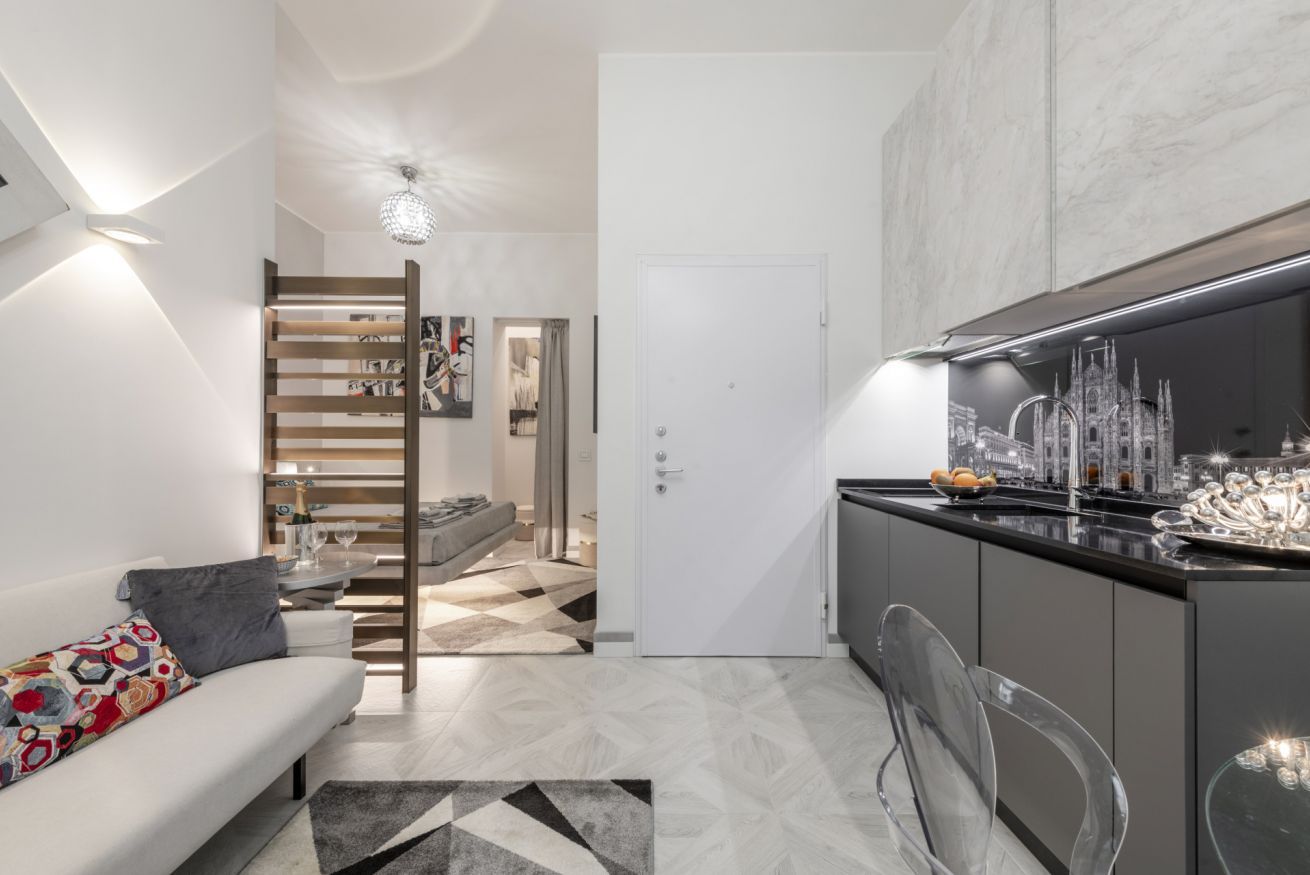 A modern kitchen with a marble countertop, a dining area with a glass table, and a living space with a sofa and a patterned rug.