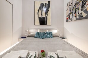 A modern hotel room with a large bed, two bedside tables, a wall-mounted artwork, and a single red rose on the bed.