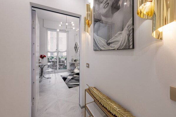 A hallway with a glass door leading to a dining area, a gold decorative console, and a framed artwork on the wall.