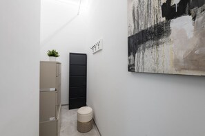 A narrow hallway with a beige cabinet, a black storage unit, a small round stool, and a large abstract painting on the wall.