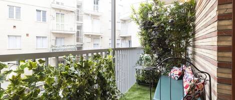 A balcony with artificial grass, a metal bench with cushions, and a potted plant.