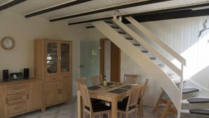 Un comedor con mesa y sillas de madera, un mueble con puertas de cristal y una escalera con barandillas blancas.