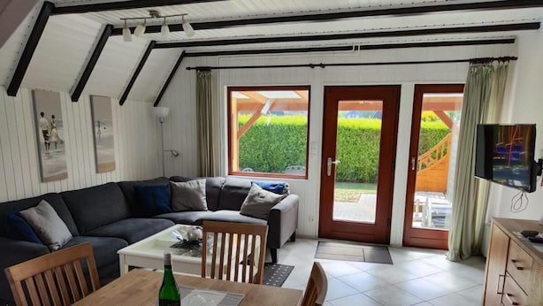 Una sala de estar acogedora con sofá, mesa de comedor y sillas. Hay un televisor montado en la pared y una ventana con vistas a zonas verdes.