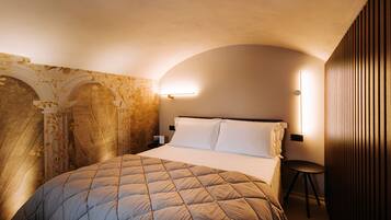 A hotel room with a bed, a small table, and a wall-mounted light fixture.