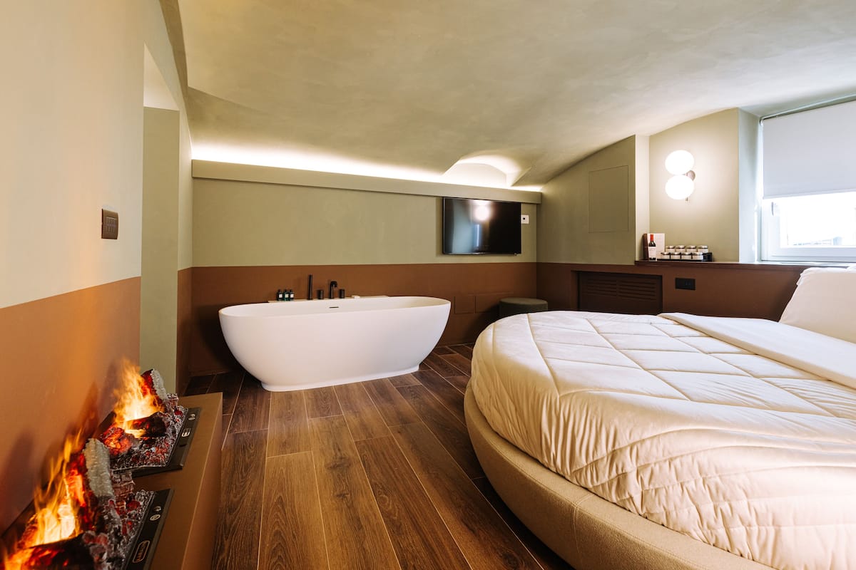 A modern bathroom with a freestanding bathtub, a large bed, and a fireplace.