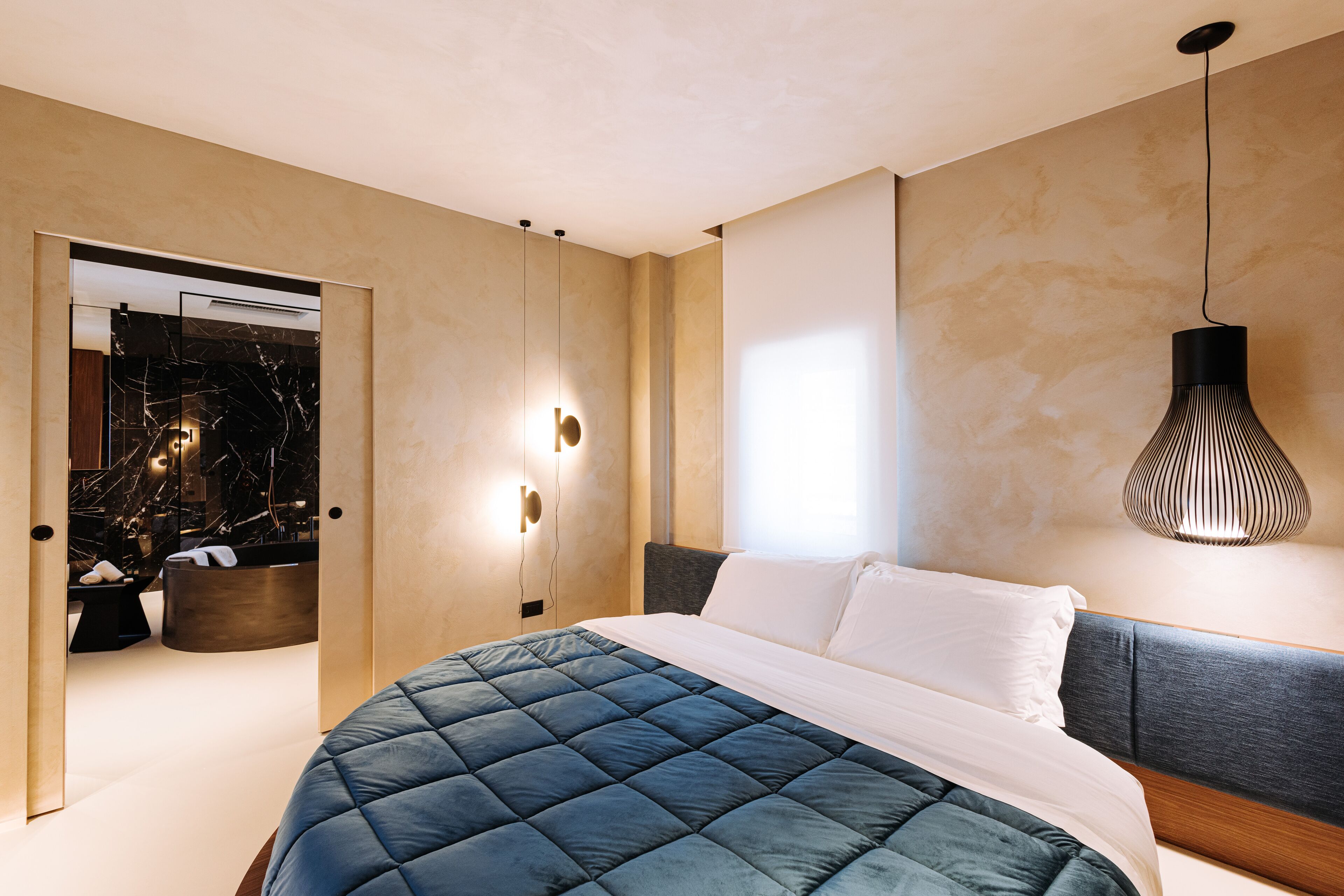 A modern bedroom with a large bed, a bedside table, a mirror, and a hanging light fixture.