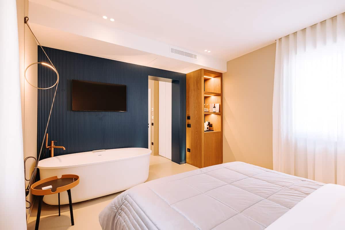 A modern bedroom with a large bed, a built-in bathtub, and a TV mounted on the wall.