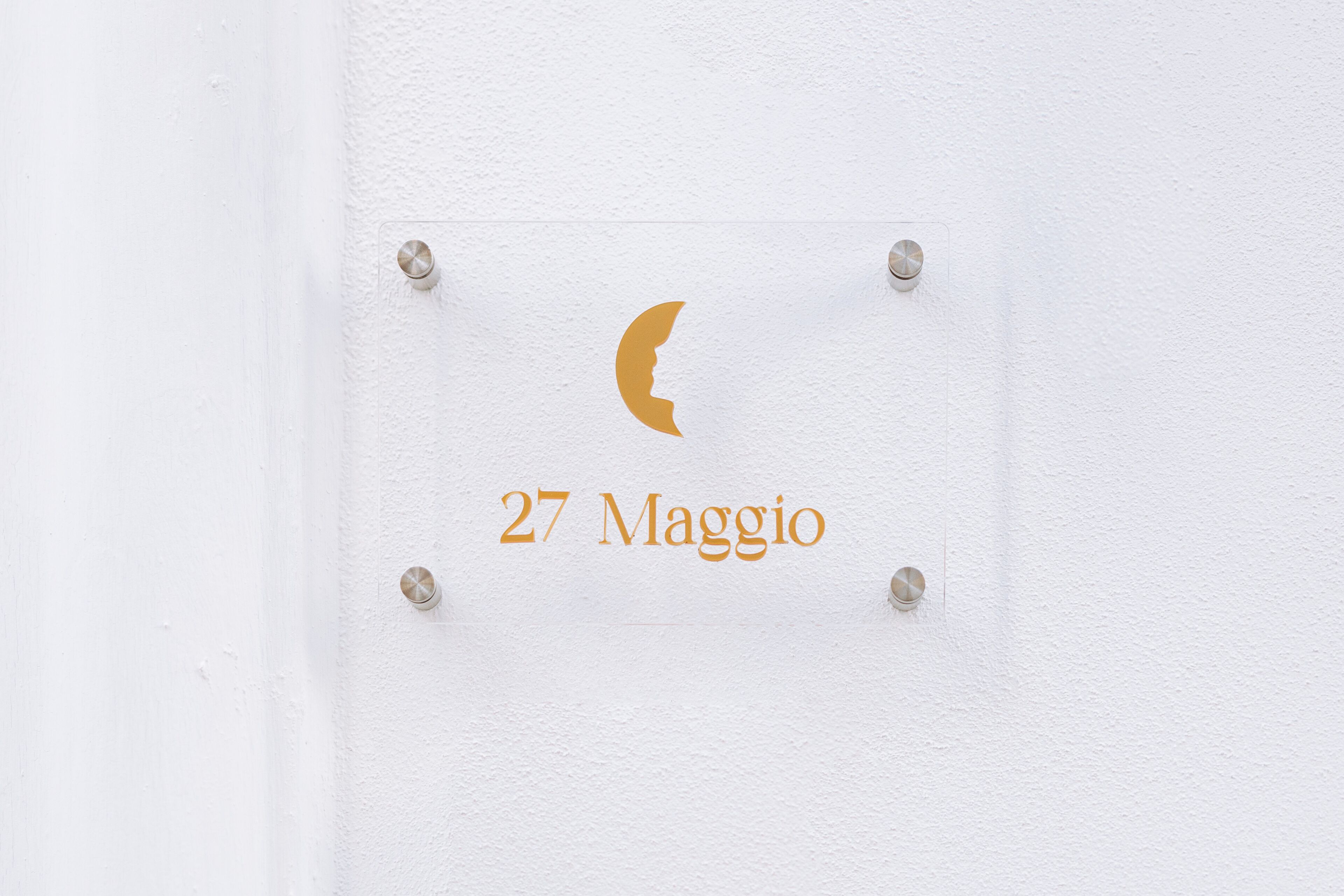 A sign with a crescent moon and the text "27 Maggio" on a white wall.