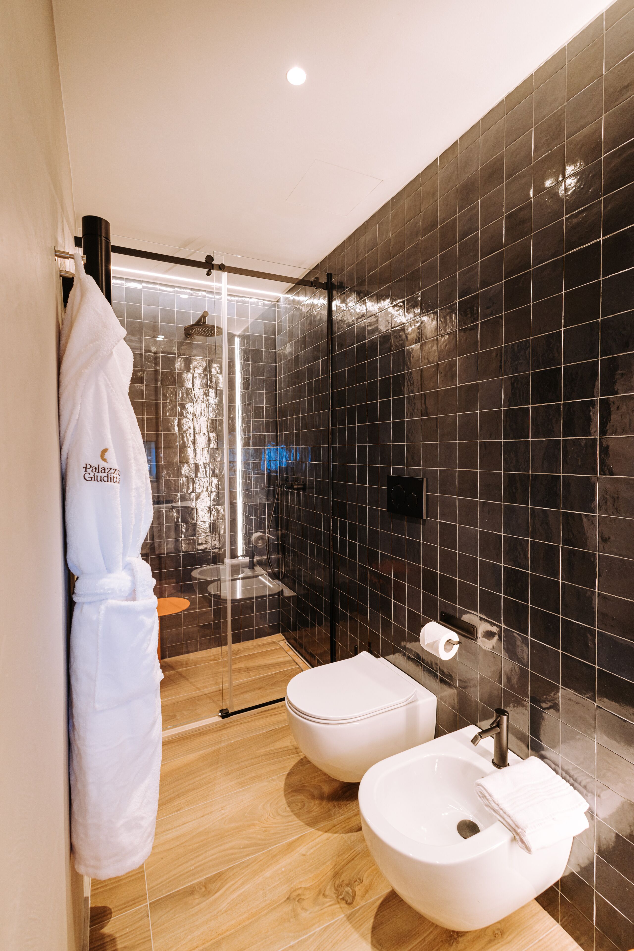 A modern bathroom with a glass-enclosed shower, two white sinks, and a robe hanging on a rack.