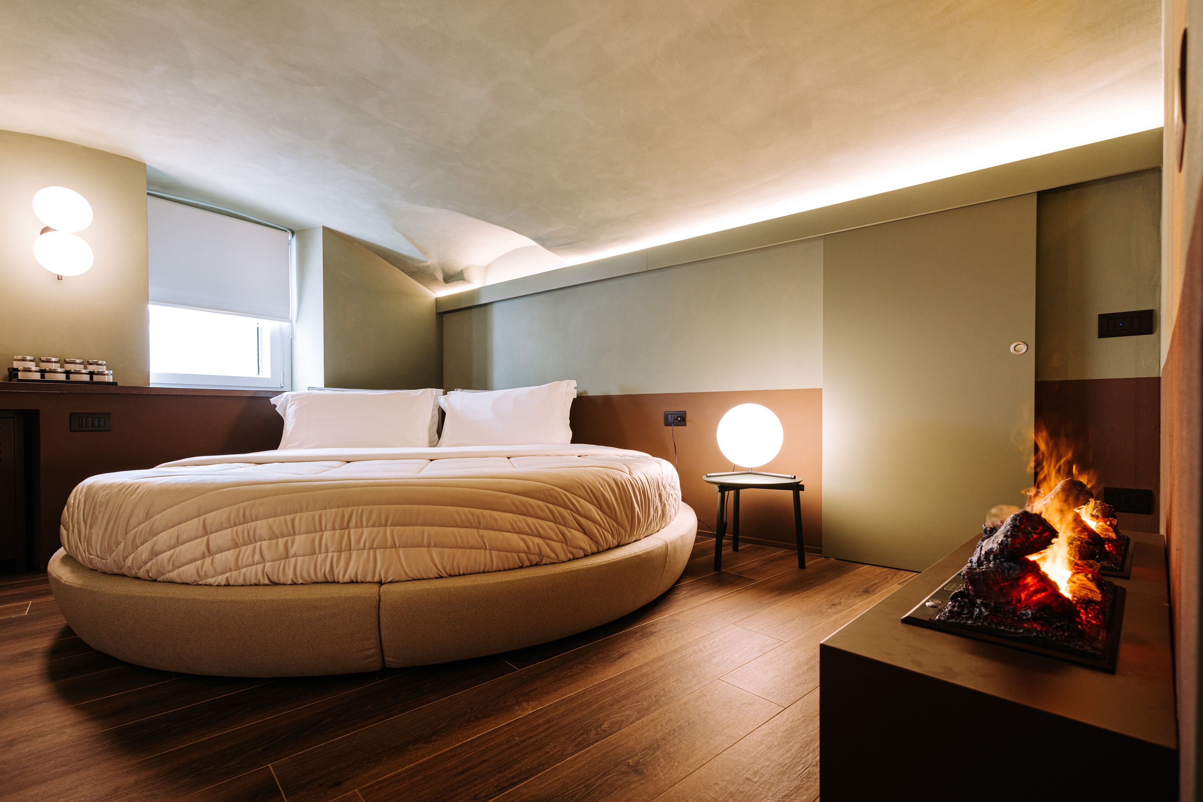 Une chambre à coucher moderne avec un lit rond, une petite table de chevet et une cheminée intégrée.