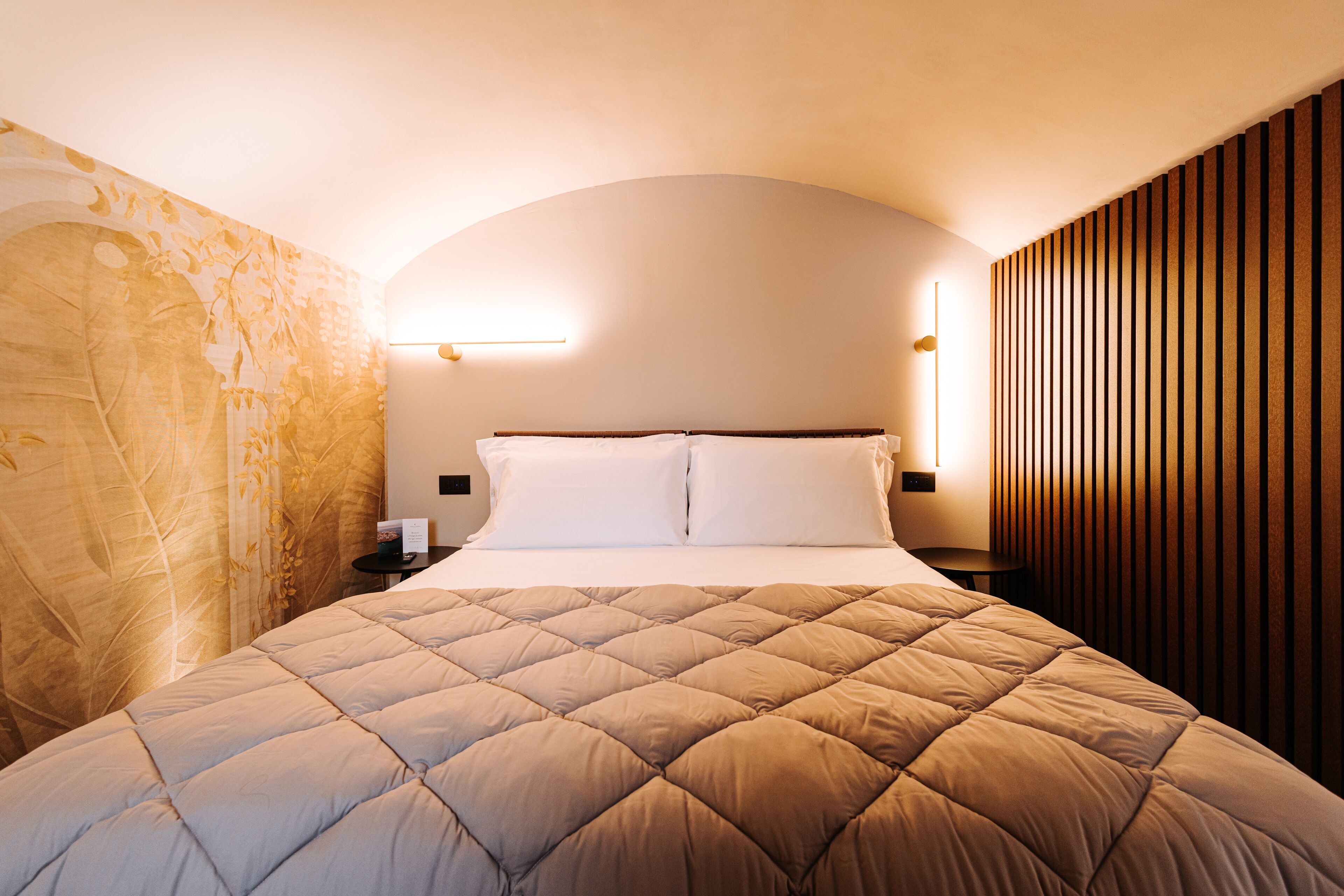 A neatly made bed with a quilted headboard, a bedside table with a lamp, and a wall with vertical wooden slats.