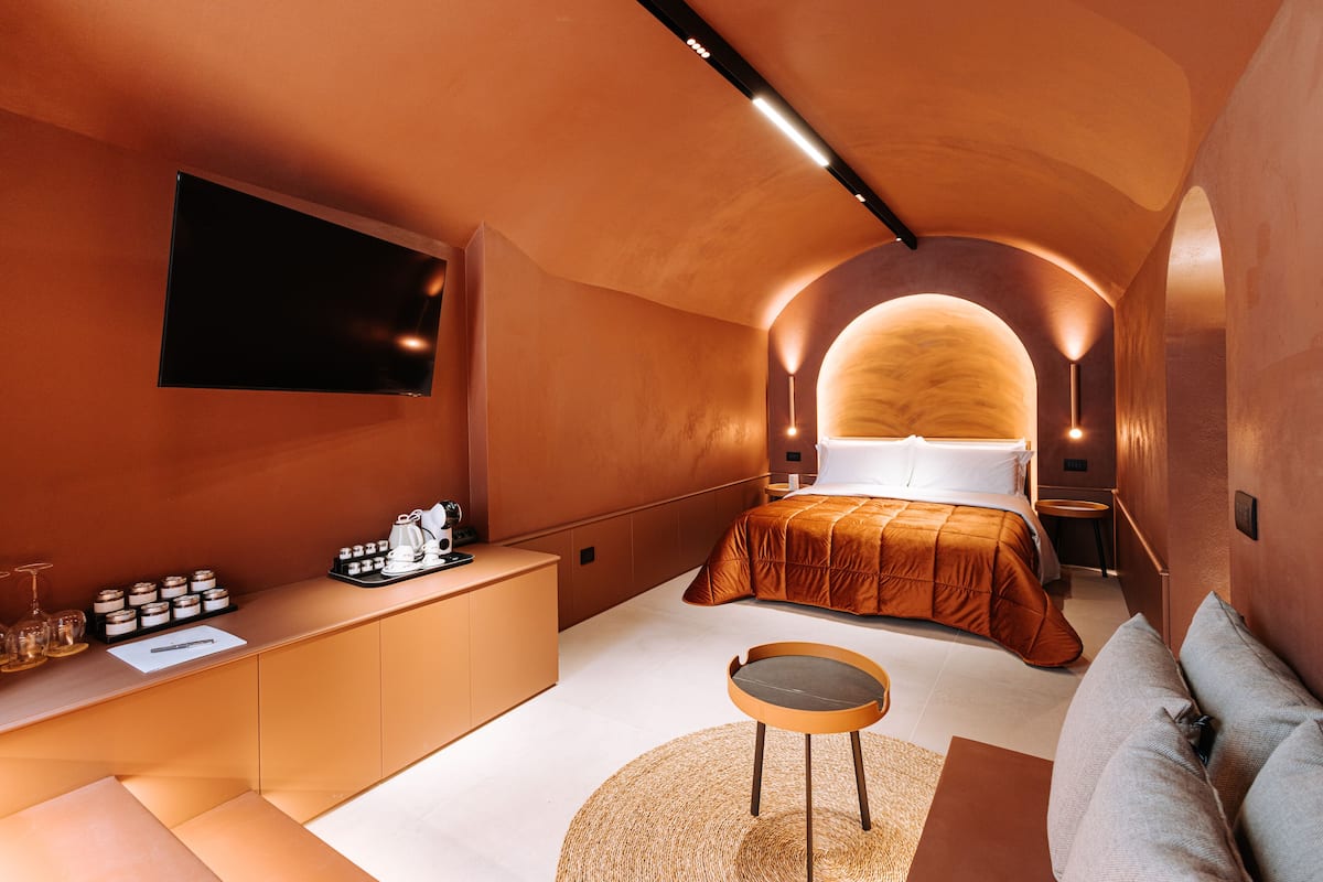 A modern bedroom with a bed, a bedside table, a TV, and a seating area.