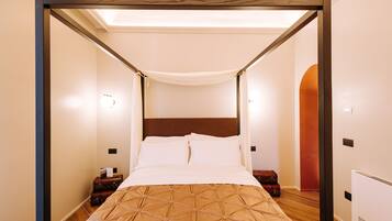 A four-poster bed with a canopy, wooden headboard, and a brown patterned bedspread. There are two bedside tables with lamps and a suitcase on one of them.