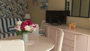 A room with a round table, a sofa, a TV, a dresser, and a vase with flowers.