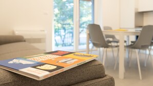 A book titled 'COSE COSI COSE CO' on a grey couch in a modern living room with a dining area in the background. - Residence Mare Azzurro (Duino-Aurisina)